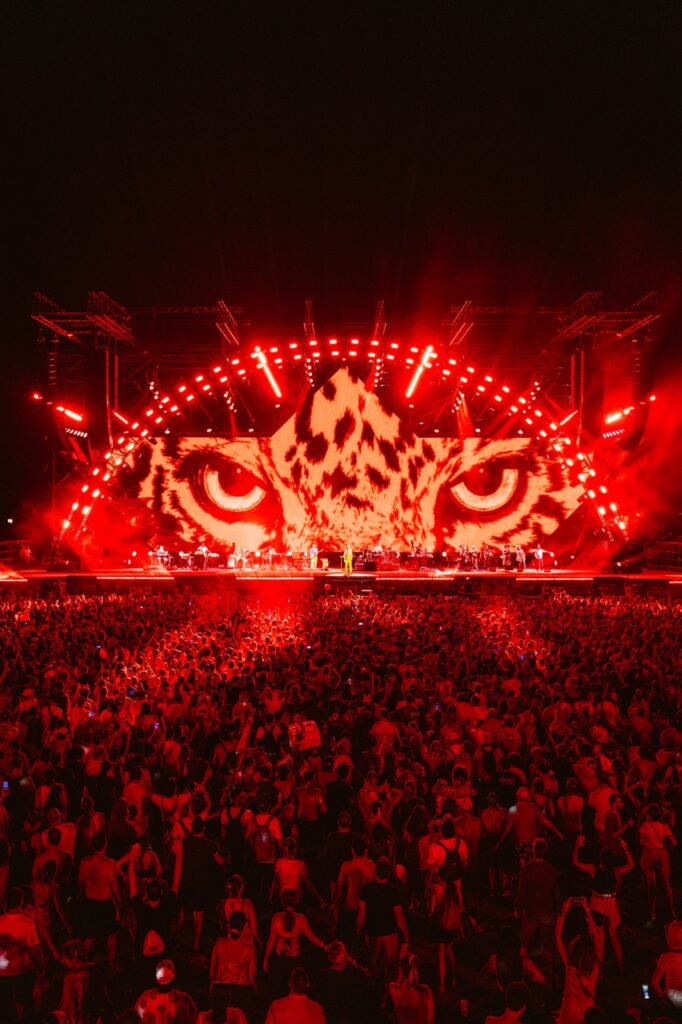 Vista panoramica del palco del Jova Summer Party di notte, illuminato da una spettacolare luce rossa e proiettori Chauvet. Sul grande LED Wall centrale sono proiettati gli occhi di un felino davanti a una numerosa folla.