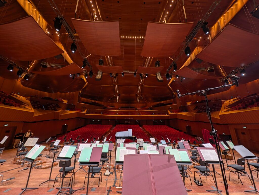 Palco con leggii per orchestra e poltrone rosse della sala da concerto.